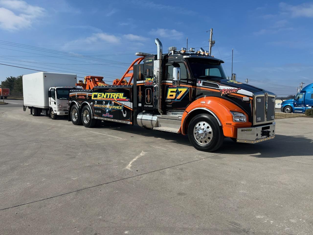 black and orange tow truck pulling baking truck