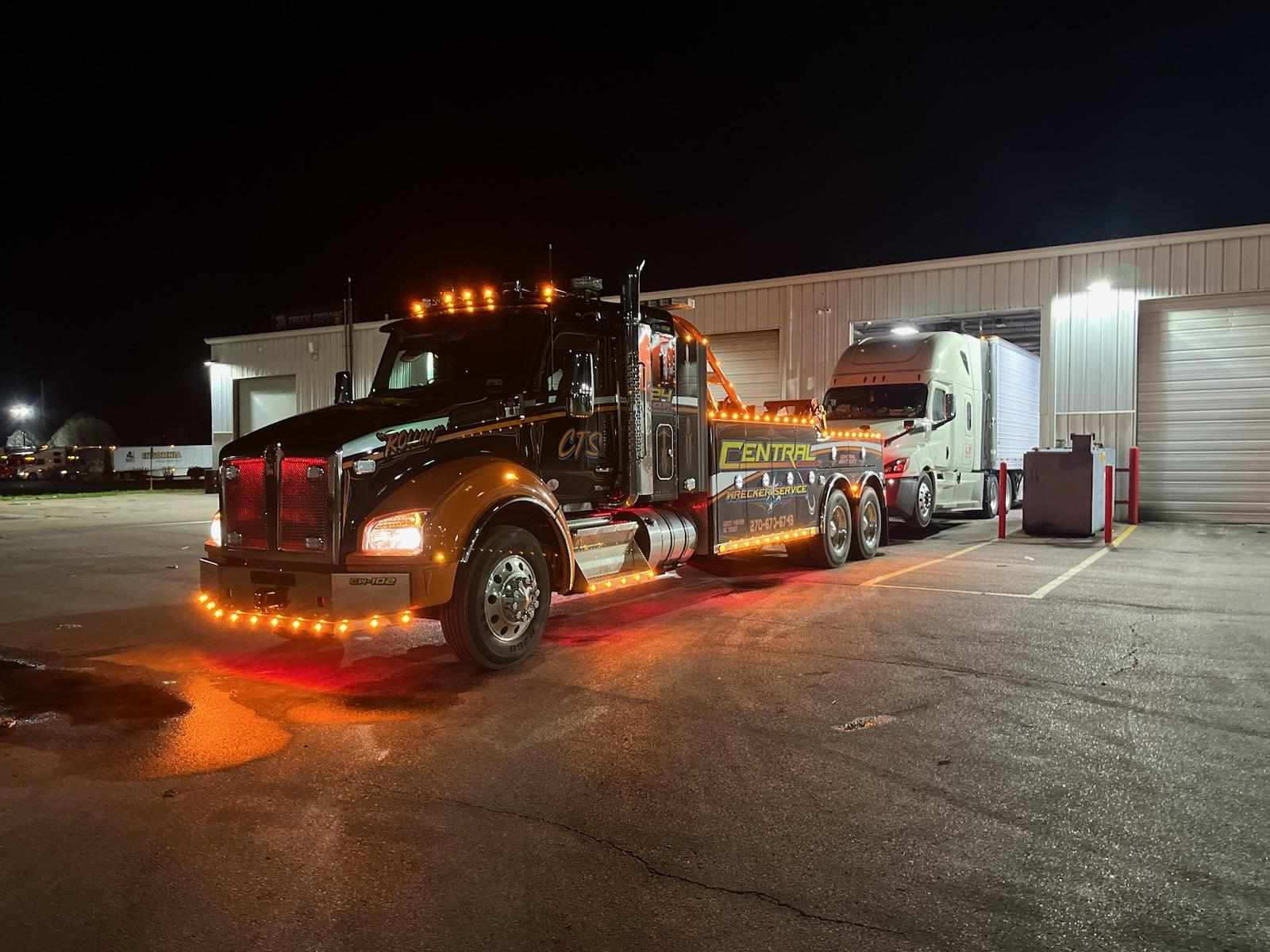 black and orange towing truck pulling semi truck at night